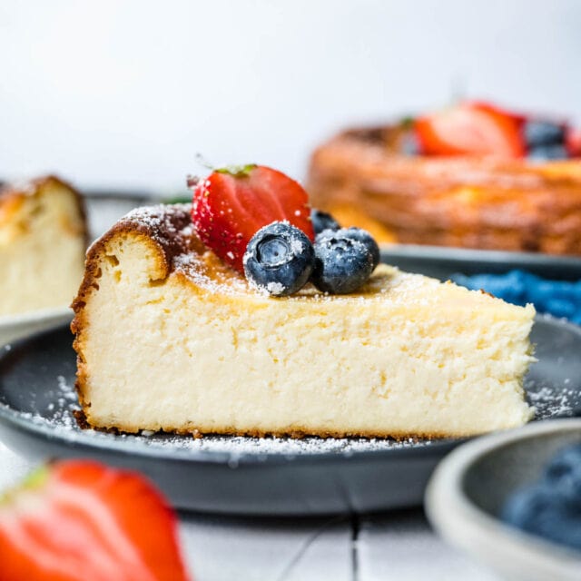 Ricotta Cheesecake slice on serving plate with fresh berries and powdered sugar on top