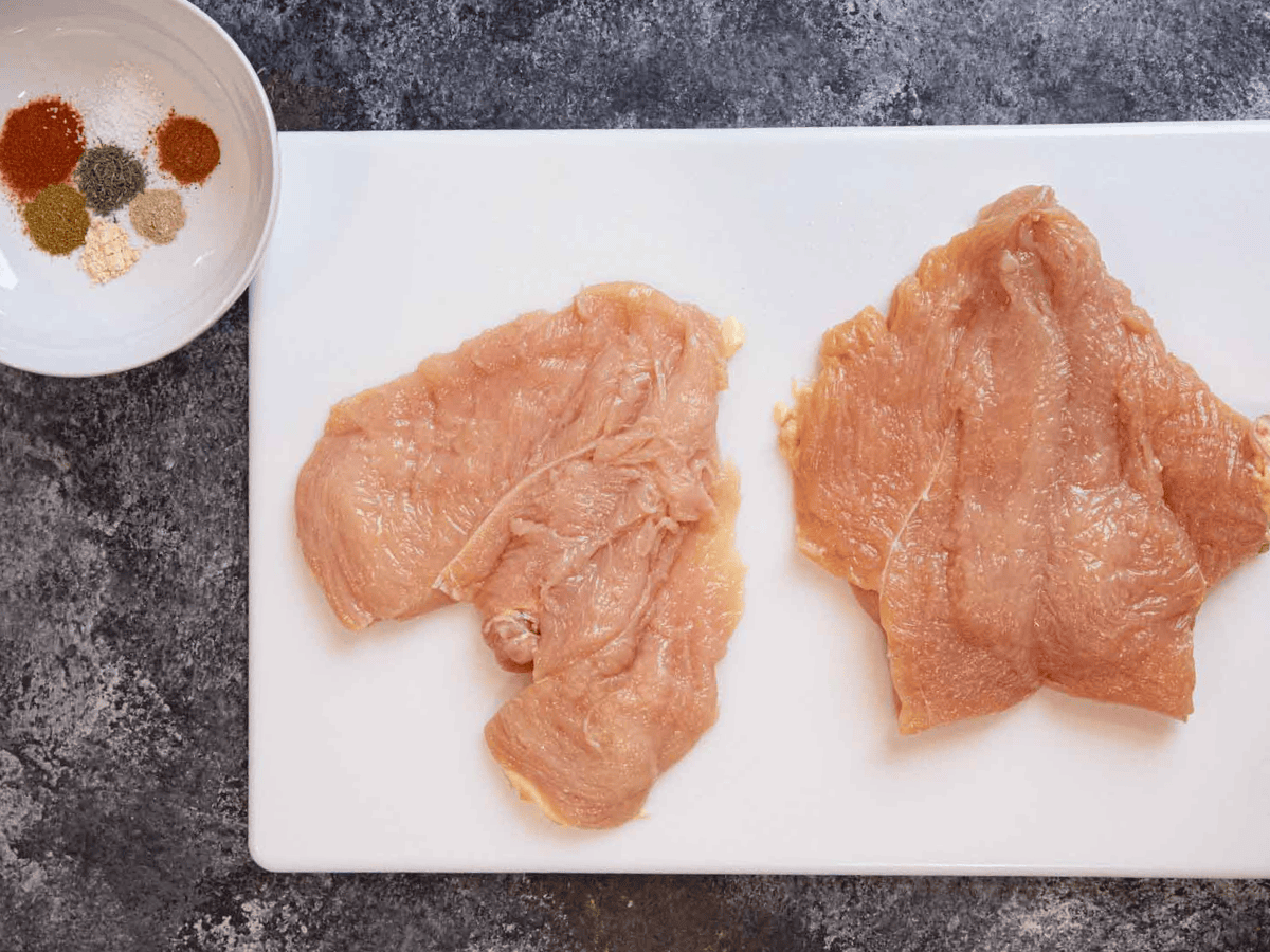 raw chicken on cutting board with seasonings in a bowl next to it