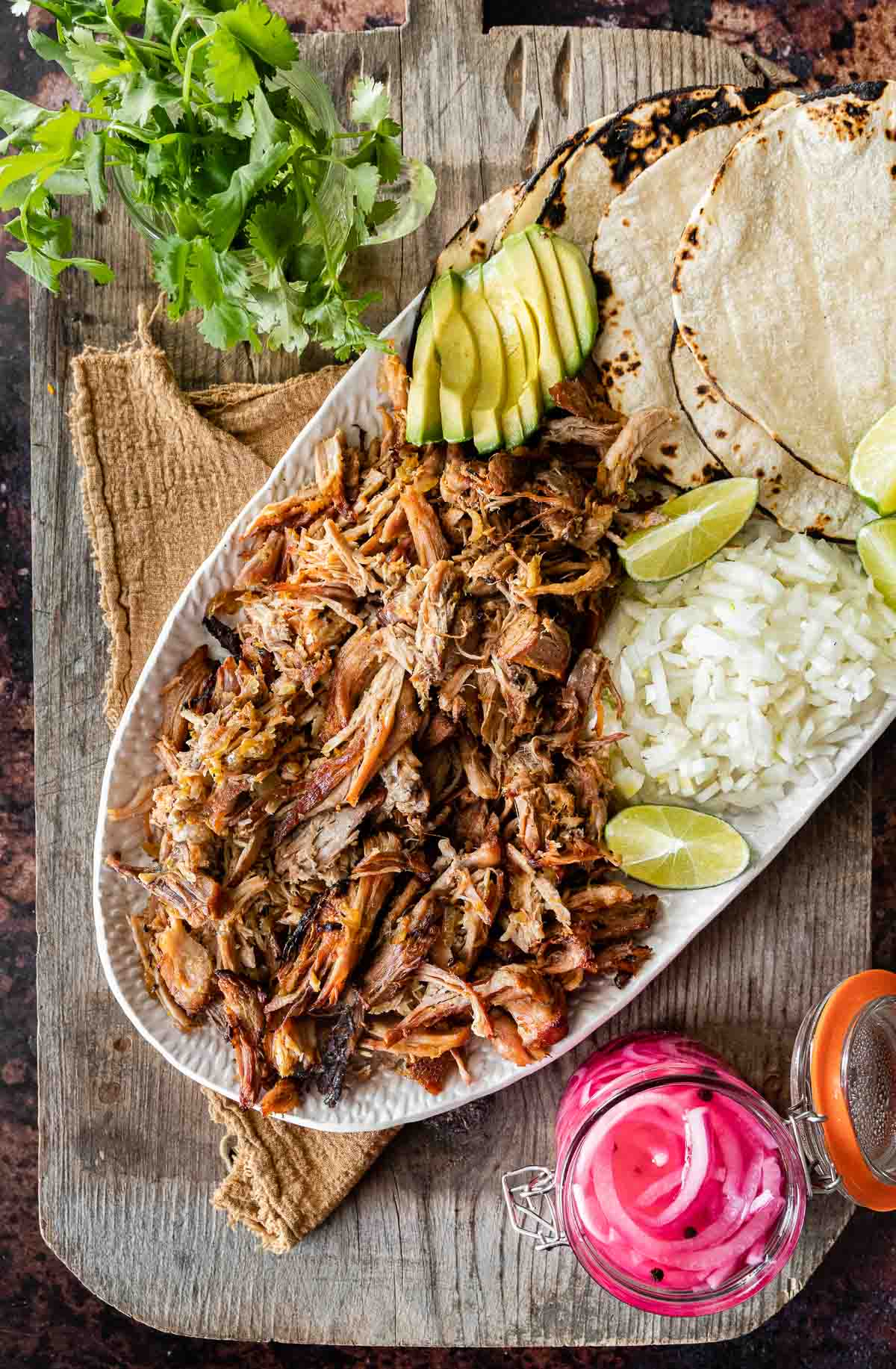 Pork Carnitas (Oven) on serving dish with rice, tortillas, limes, avocado, and pickled onions