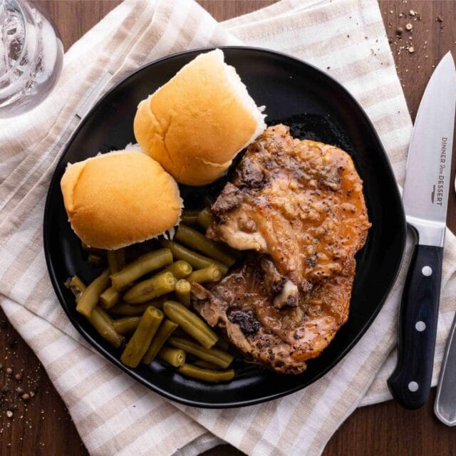 Slow Cooker Pork Chops on plate with green beans and dinner rolls