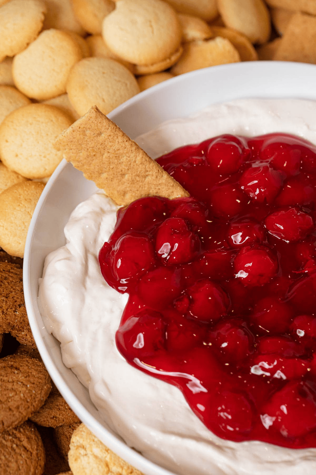 cream cheese and cherry pie filling in a bowl with a graham cracker dipped in