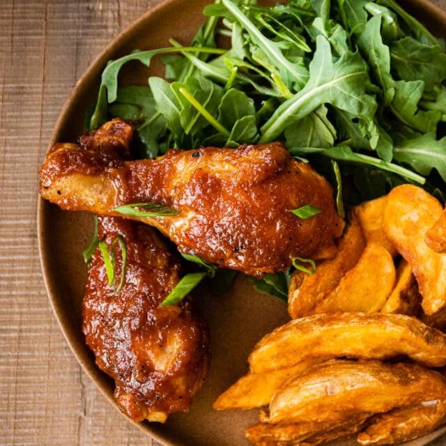 Applesauce BBQ Chicken on dinner plate with arugula salad and potato wedges