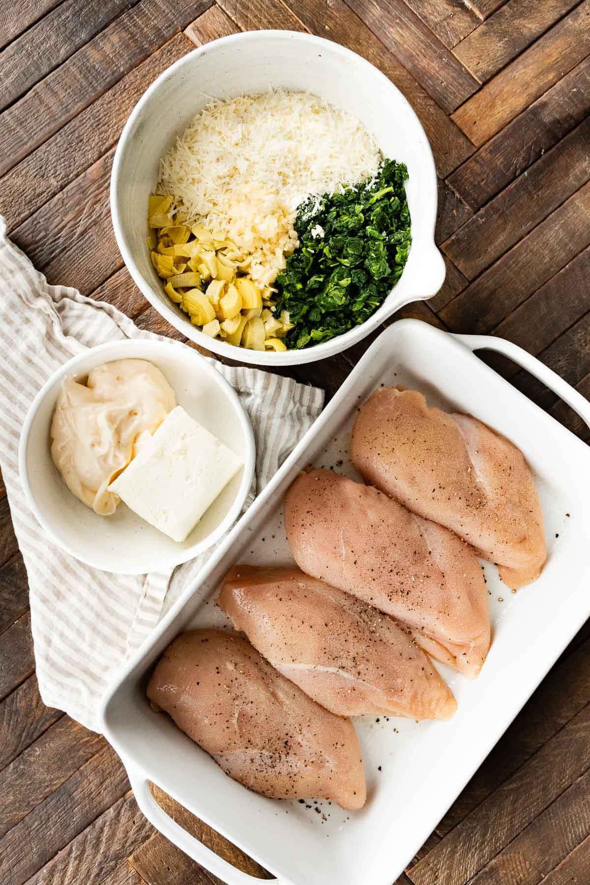 Chicken in baking dish and topping ingredients for Baked Spinach Artichoke Chicken