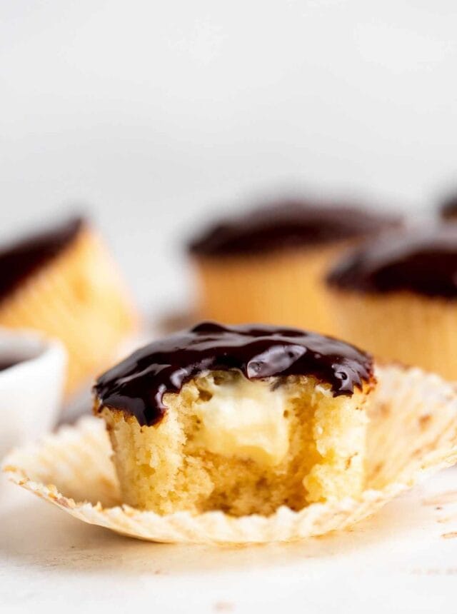 Boston Cream Cupcakes vanilla cupcake with bite exposing cream filling and chocolate ganache frosting
