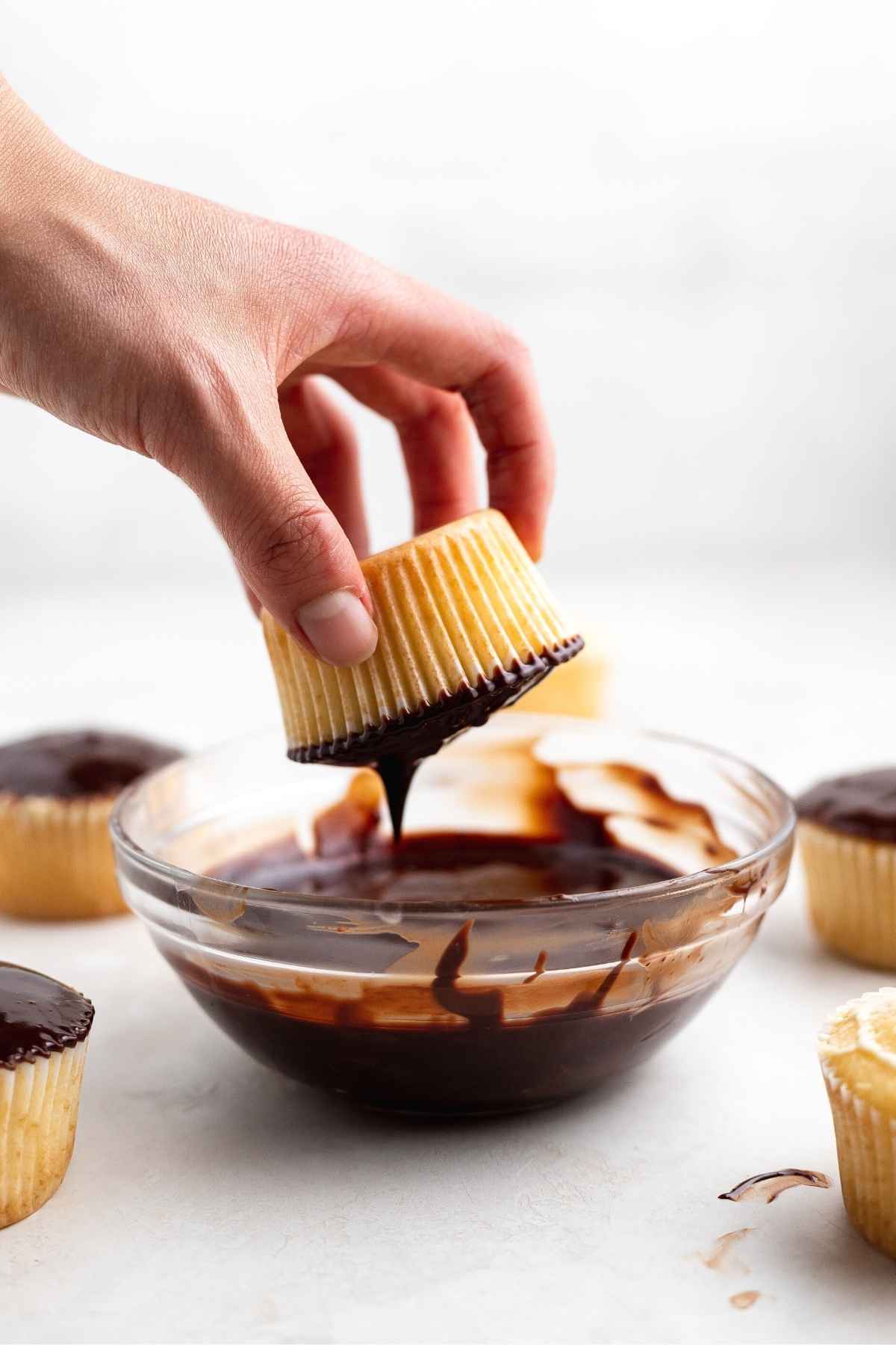 Boston Cream Cupcakes dipping filled vanilla cupcakes into chocolate ganache frosting