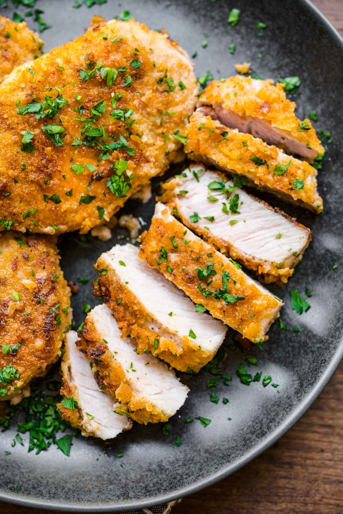 Breaded Pork Chops sliced on serving plate with chopped fresh parsley garnish