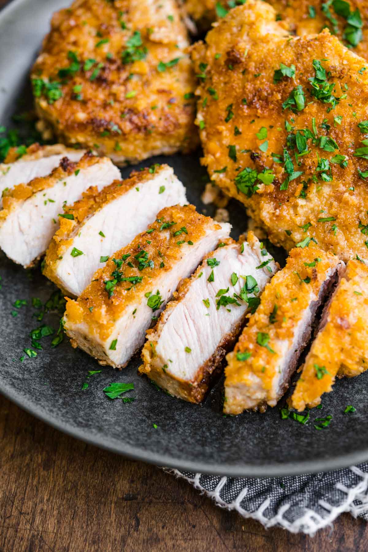 Breaded Pork Chops sliced on serving plate with chopped fresh parsley garnish