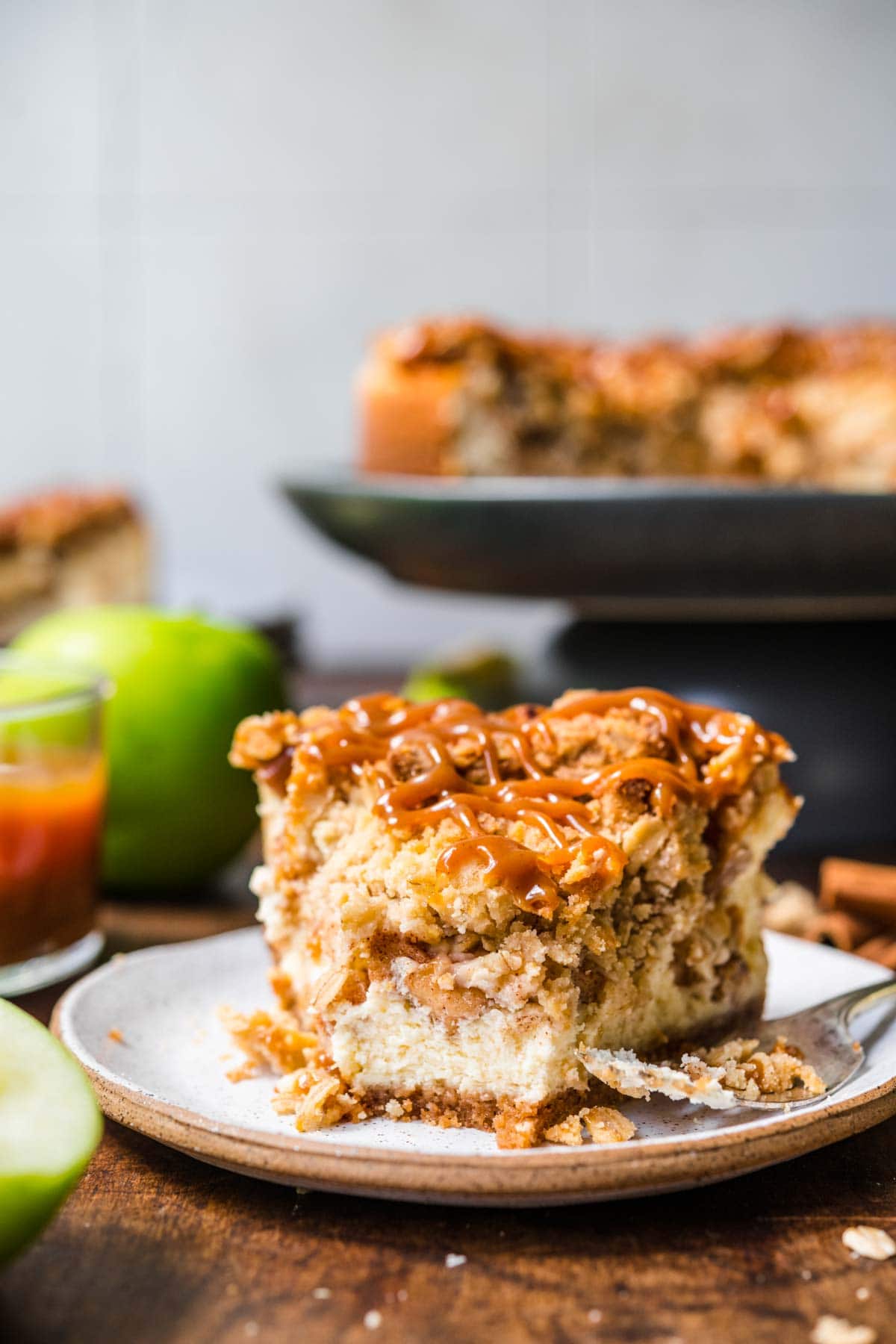 Caramel Apple Crumb Cheesecake slice on plate with caramel drizzle on top and fork