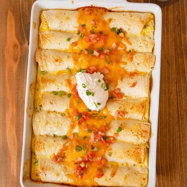Cheesy Breakfast Enchiladas in baking dish topped with cheese, salsa, and sour cream