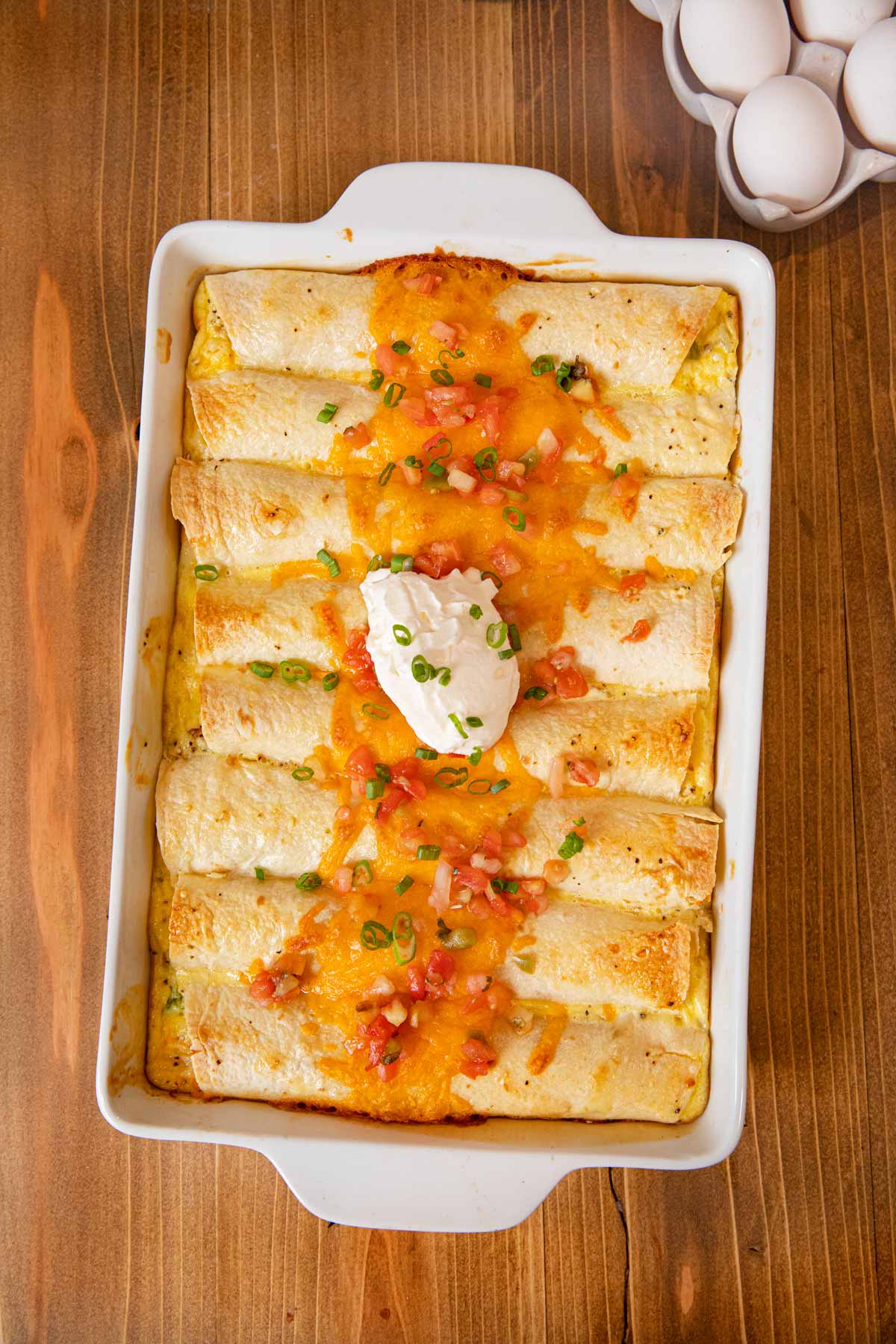 Cheesy Breakfast Enchiladas in baking dish topped with cheese, salsa, and sour cream