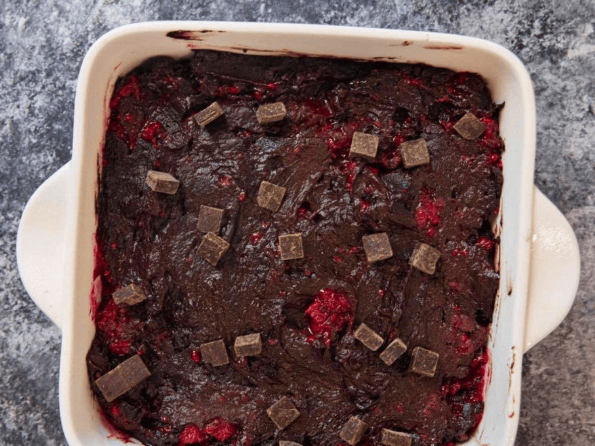 Brownie batter in pan with chocolate chunks and raspberries