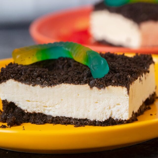 Serving of cake topped with gummy worm on yellow plate