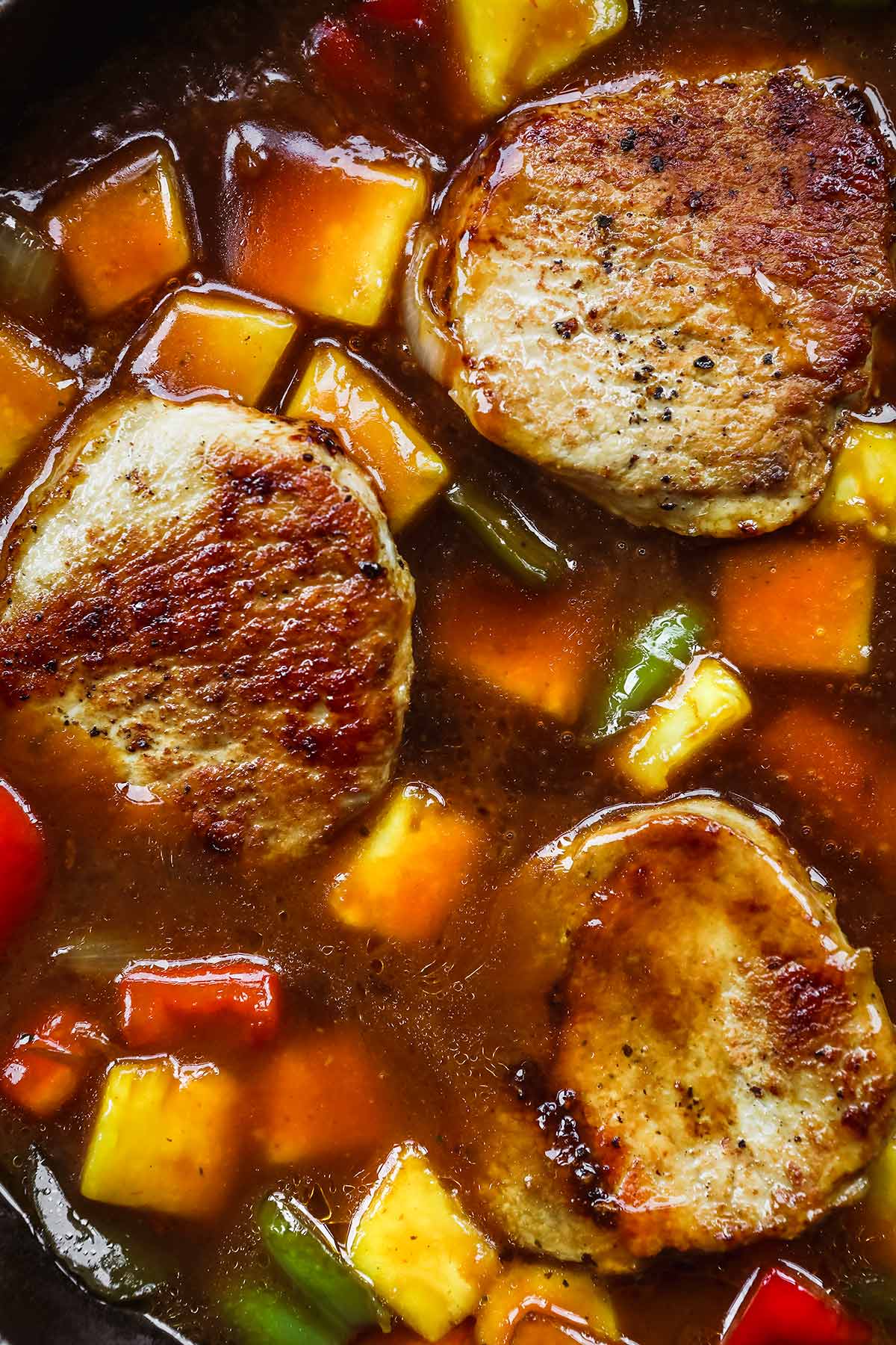 Hawiian Pork Chops simmering in sauce with pineapples, onions, and bell peppers