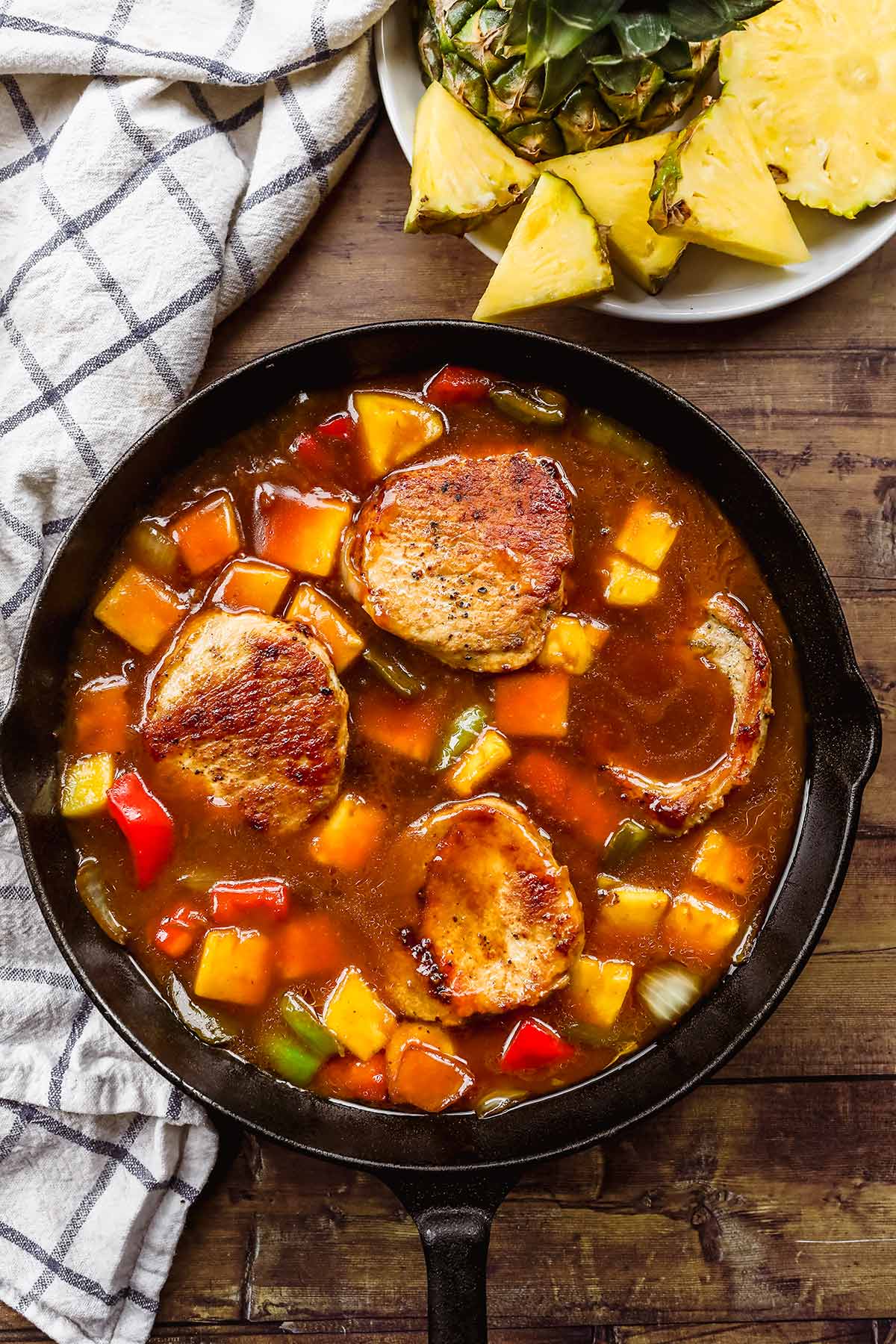 Hawiian Pork Chops simmering in sauce with pineapples, onions, and bell peppers