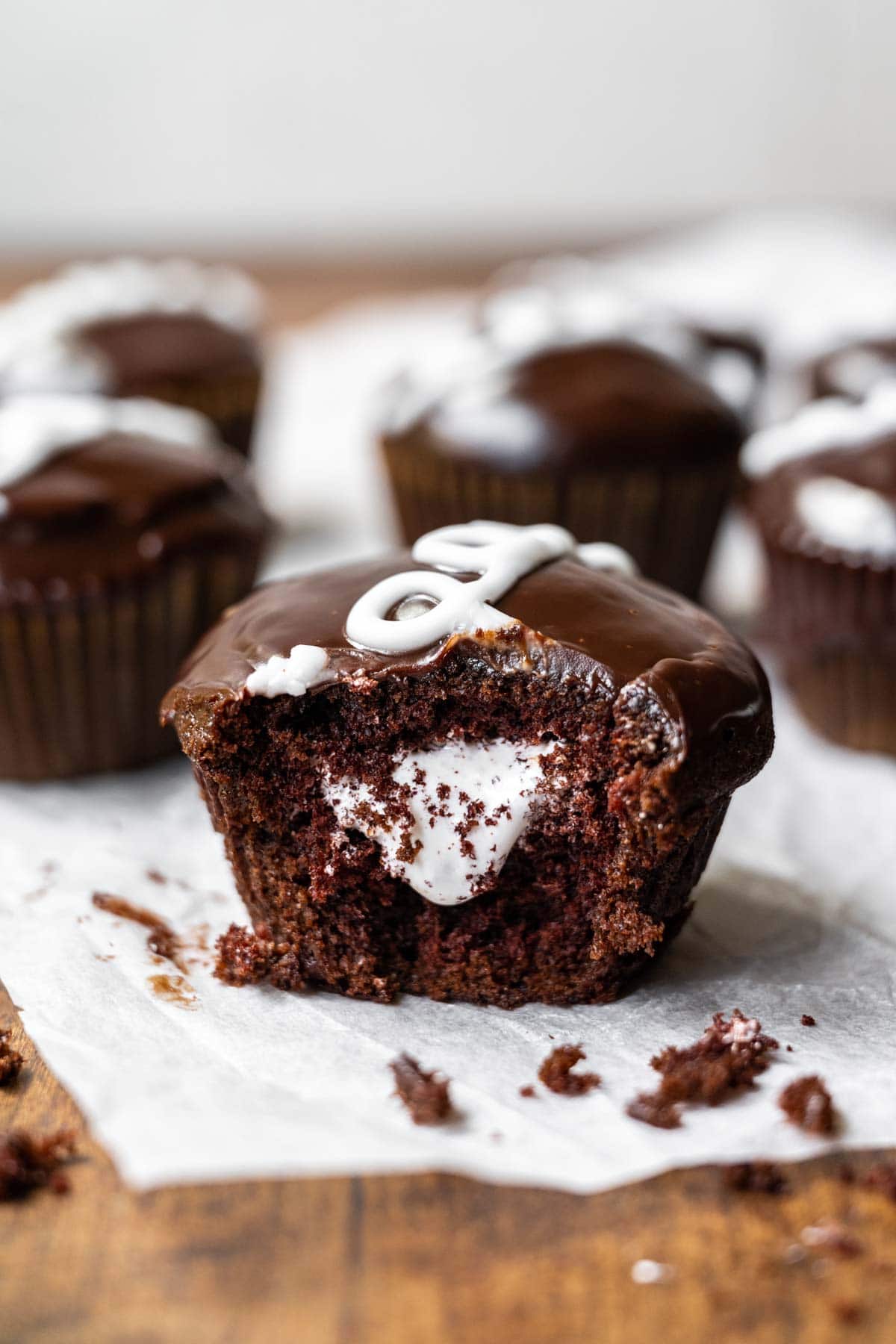 Hostess Cupcakes (Copycat) chocolate cupcake with marshmallow filling and ganache icing with white swirl on parchment paper 