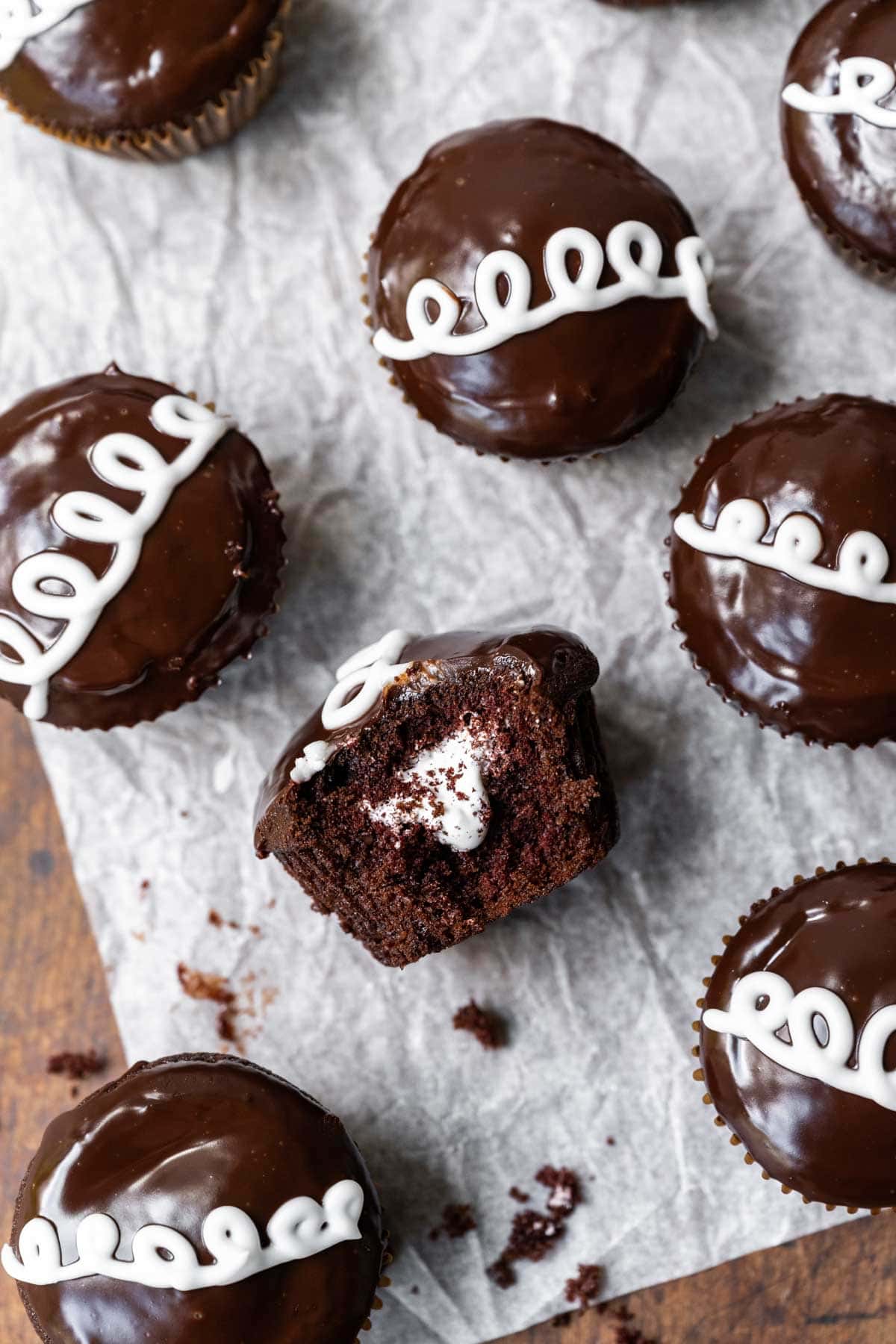 Hostess Cupcakes (Copycat) chocolate cupcake with marshmallow filling and ganache icing with white swirl on parchment paper
