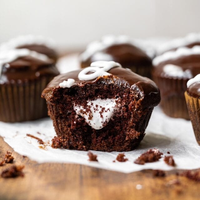Hostess Cupcakes (Copycat) chocolate cupcake with marshmallow filling and ganache icing with white swirl on parchment paper