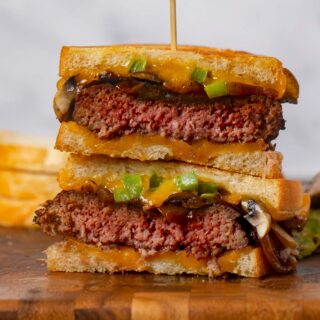 Philly Cheesesteak Patty Melt stacked sandwich halves on cutting board