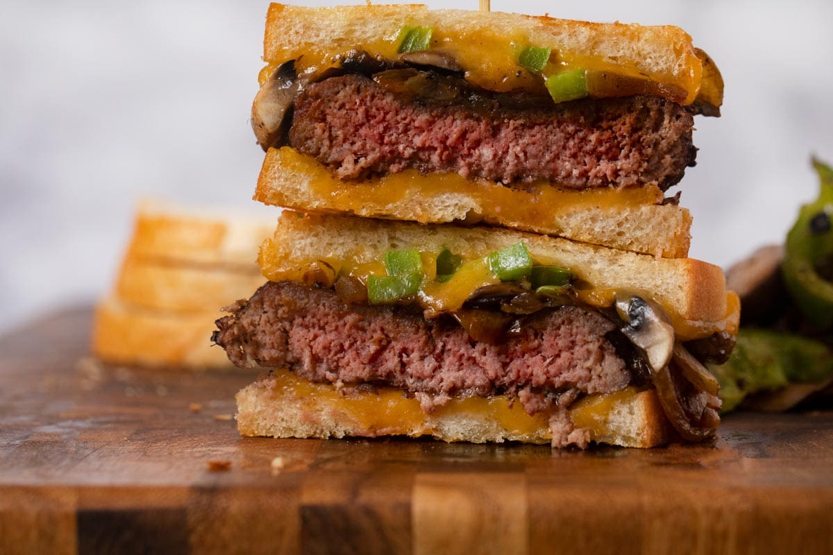 Philly Cheesesteak Patty Melt stacked sandwich halves on cutting board