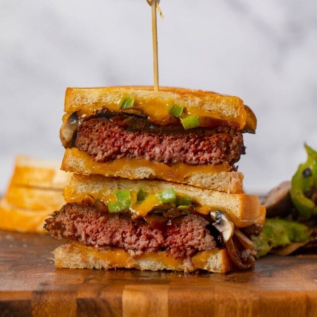 Philly Cheesesteak Patty Melt stacked sandwich halves on cutting board
