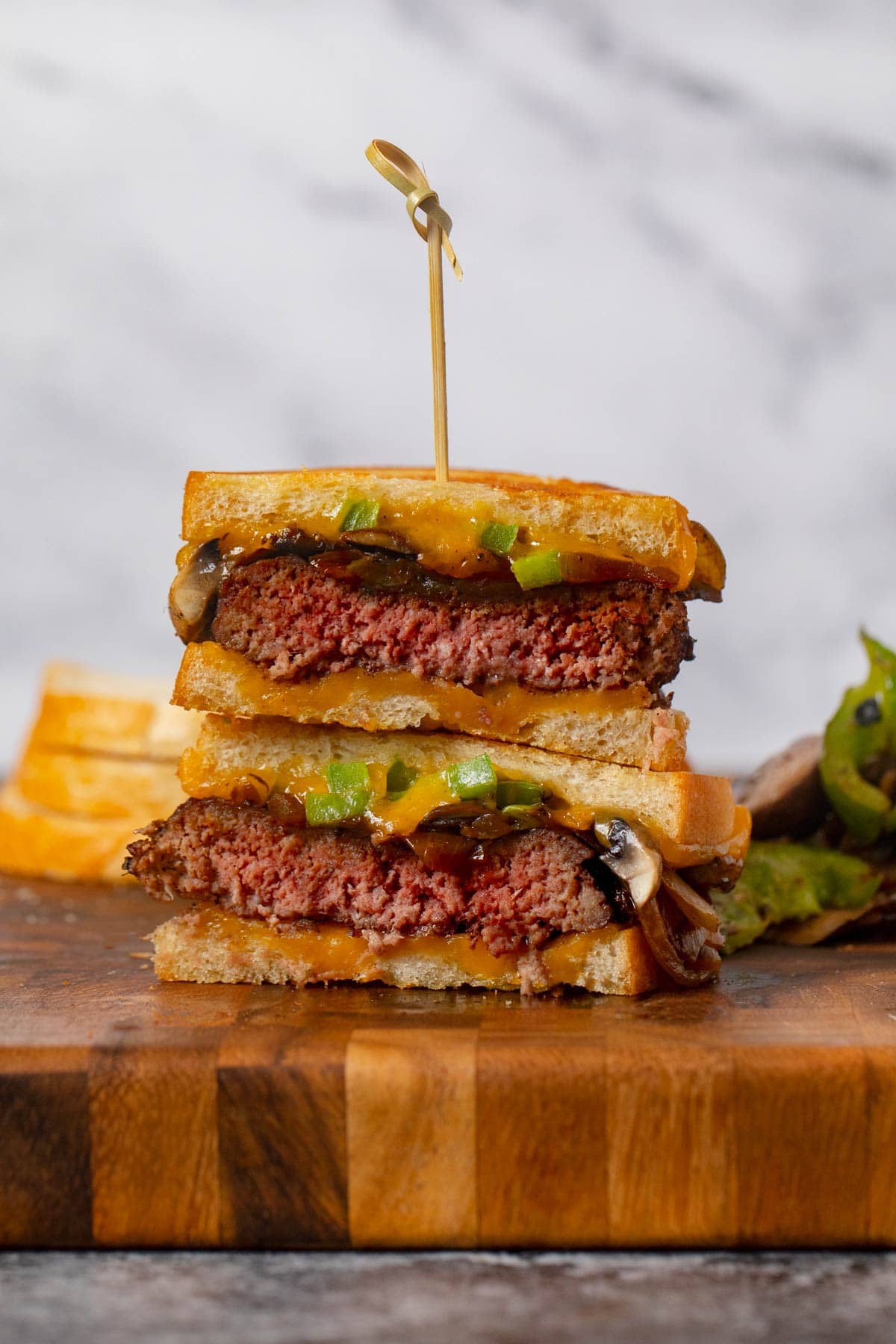 Philly Cheesesteak Patty Melt stacked sandwich halves on cutting board