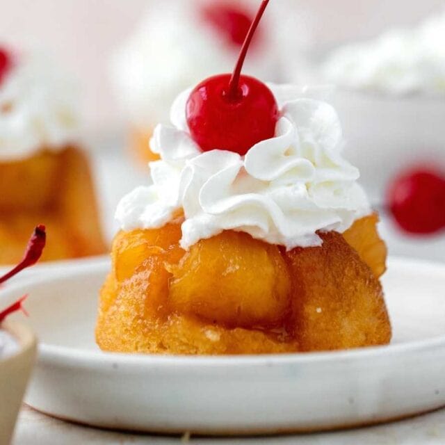 Cupcakes on serving plates with cherry and whipped cream topping.
