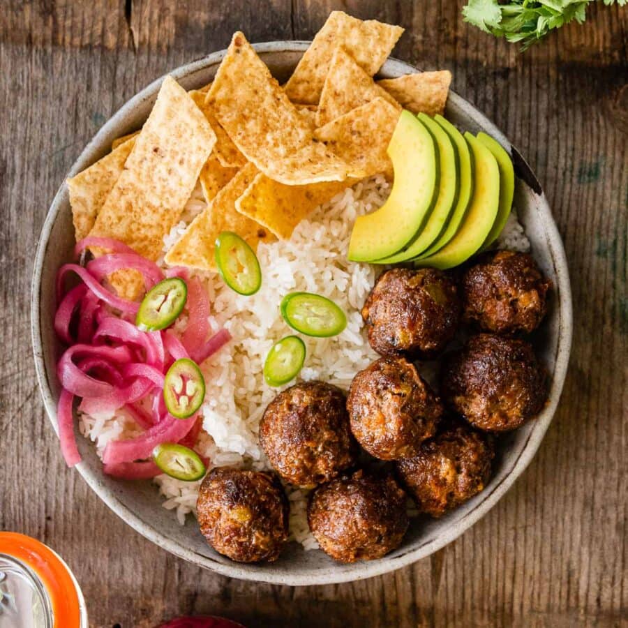 Taco Meatballs in bowl with rice, chips, avocado, jalapeƱos, and pickled onions