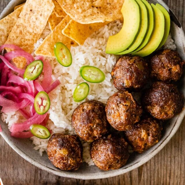 beef rounds in a bowl of rice, topped with avocado, chips, onions, and chilies.