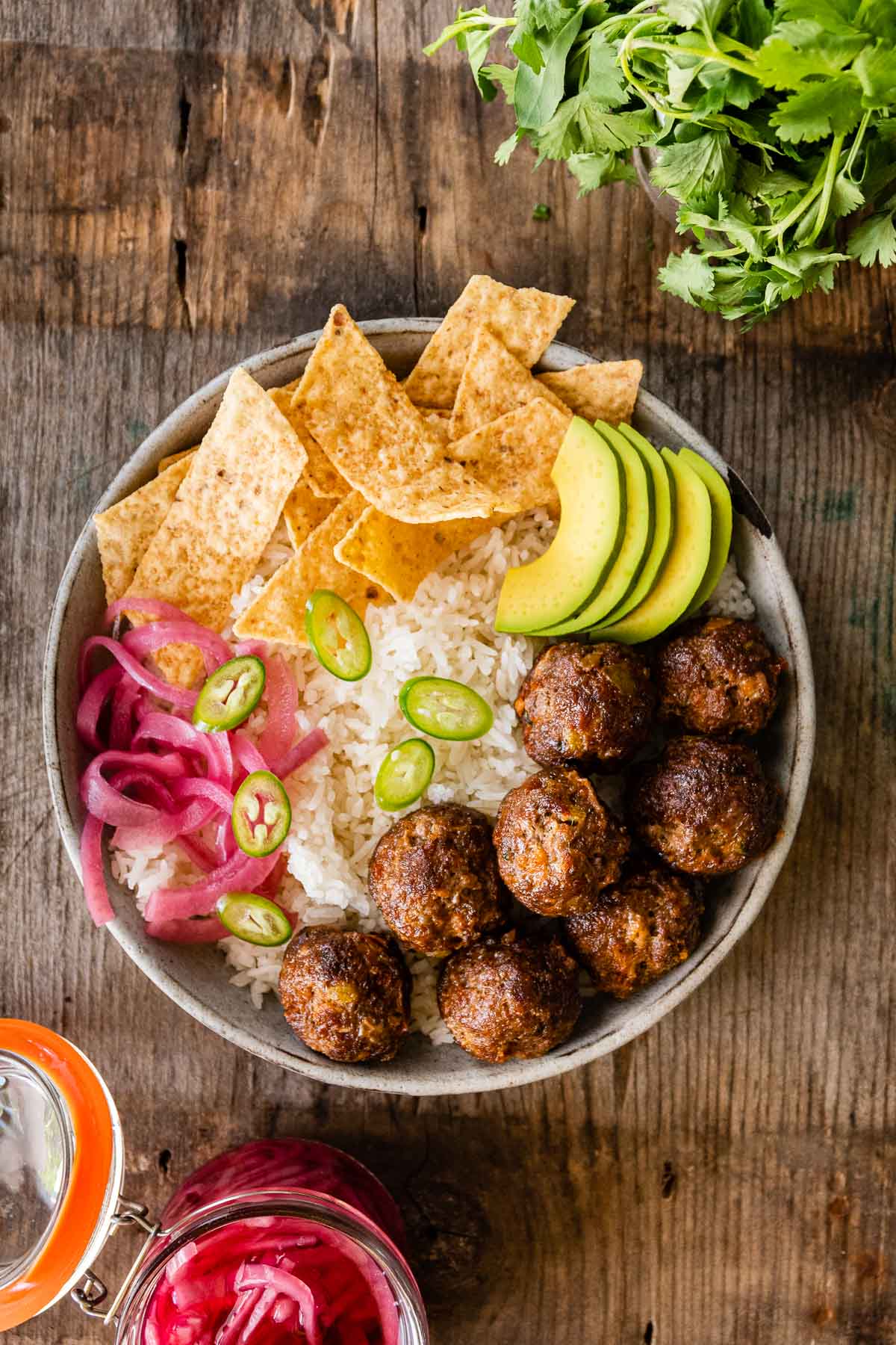 Taco Meatballs in bowl with rice, chips, avocado, jalapeños, and pickled onions