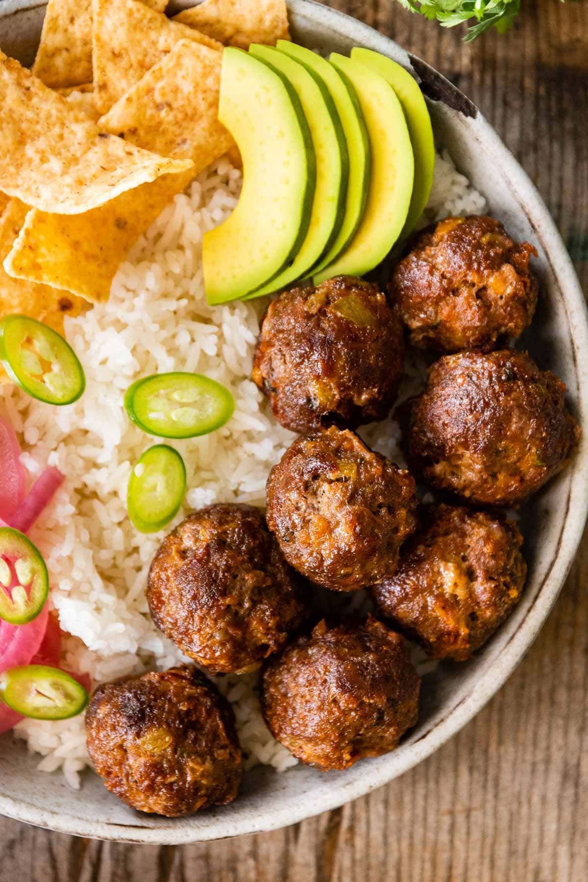 Taco Meatballs in bowl with rice, chips, avocado, jalapeños, and pickled onions