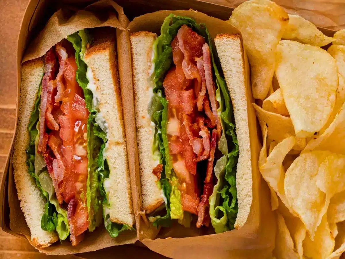 meat and veggies in between two pieces of bread cut in half with potato chips on the side