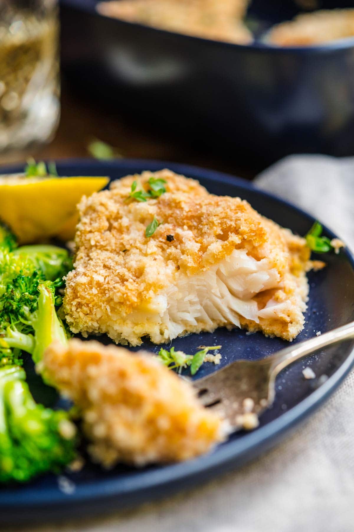 Baked Cod with lemon wedge garnish on plate with broccoli and fork
