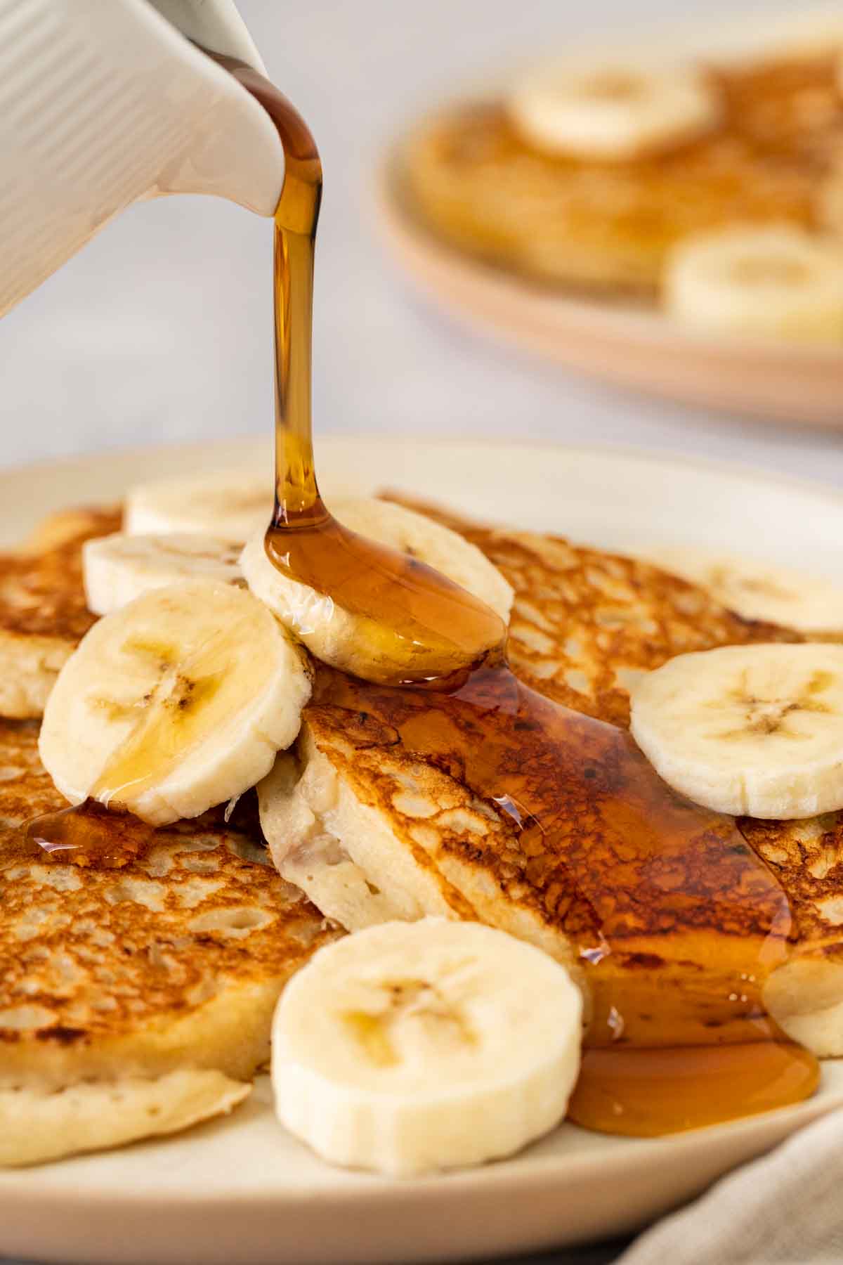 Banana Pancakes pouring syrup on pancakes on serving plate