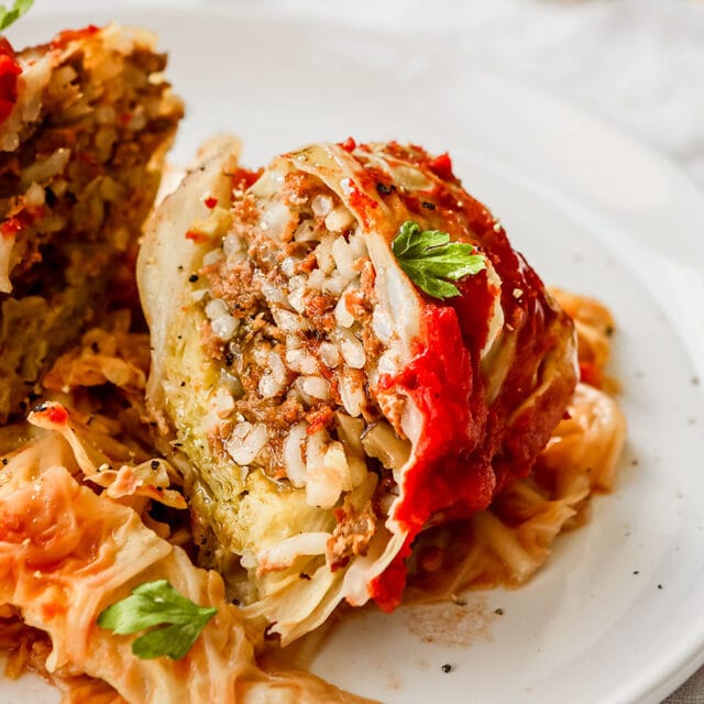cabbage leaf roll on plate with tomato sauce and parsley garnish cut open rice and beef inside 4x3