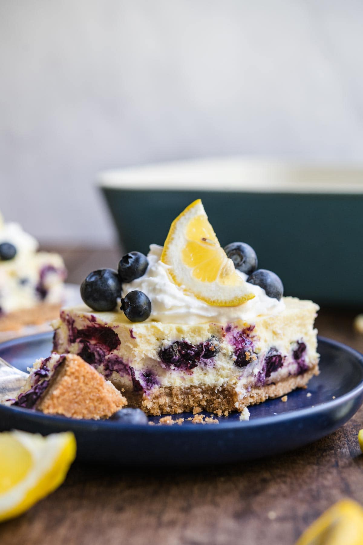 Blueberry Lemon Cheesecake Bars slice on plate garnished with whipped cream, lemon wedge, and fresh blueberries