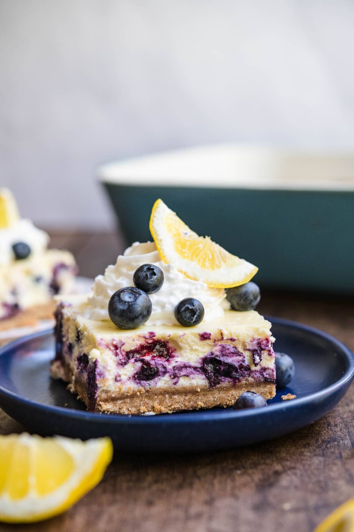 Blueberry Lemon Cheesecake Bars slice on plate garnished with whipped cream, lemon wedge, and fresh blueberries