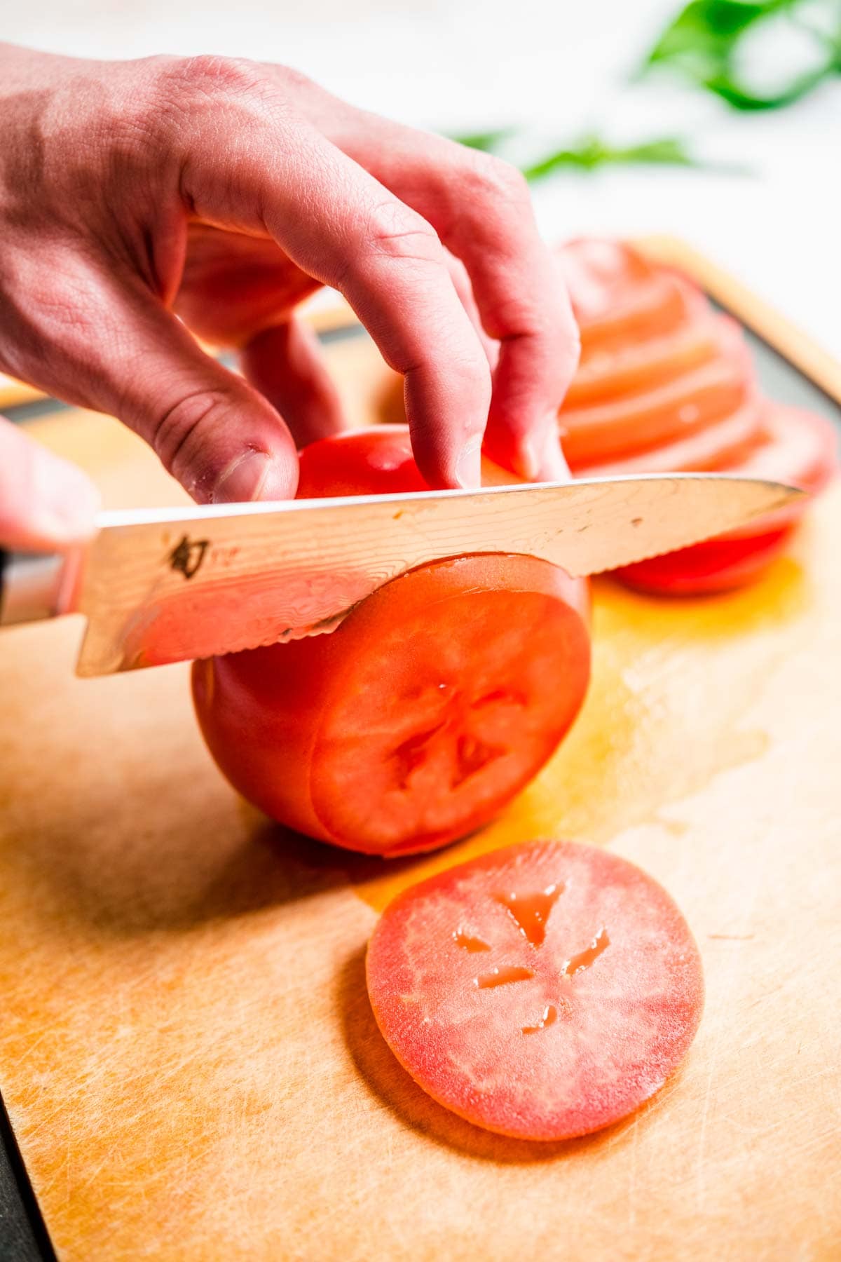 Tomato being sliced on cutting board for Tomato Mozzarella Salad