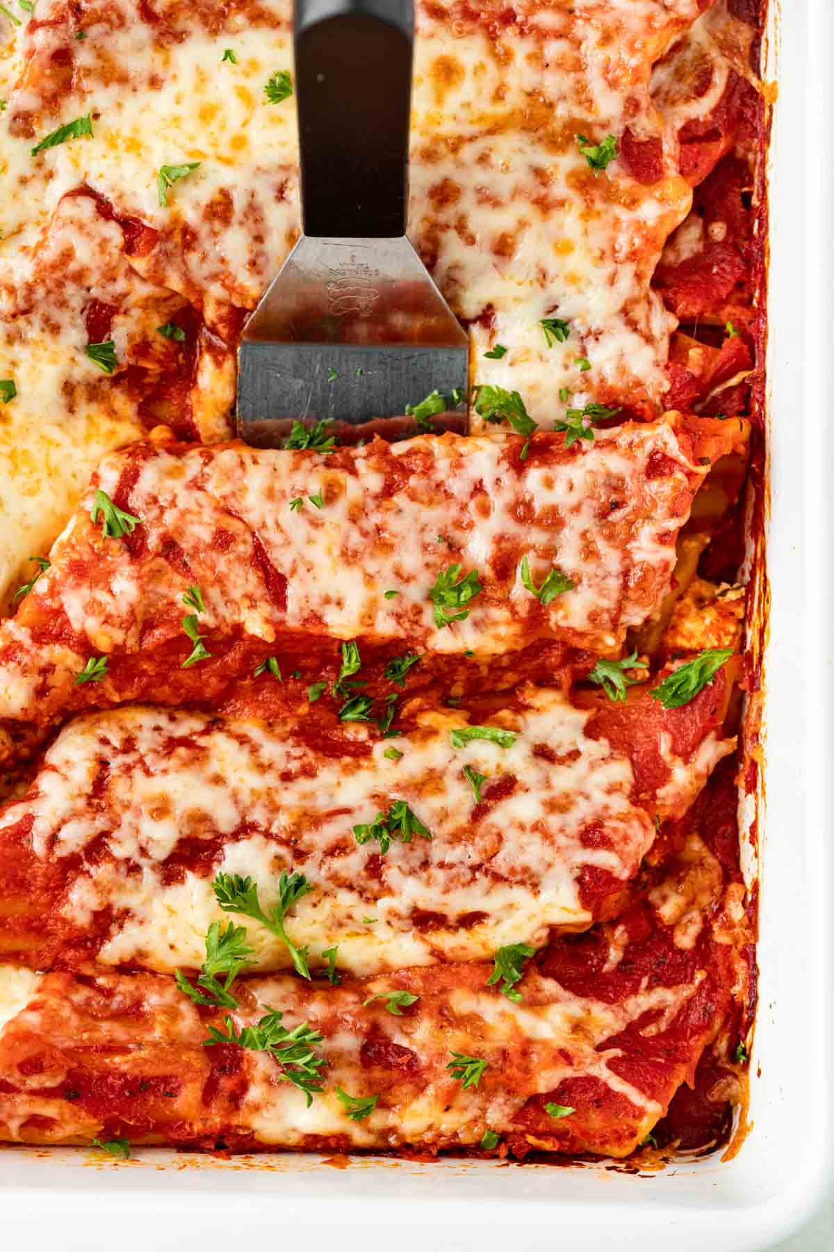 Cheesy Manicotti baked in pan with spatula