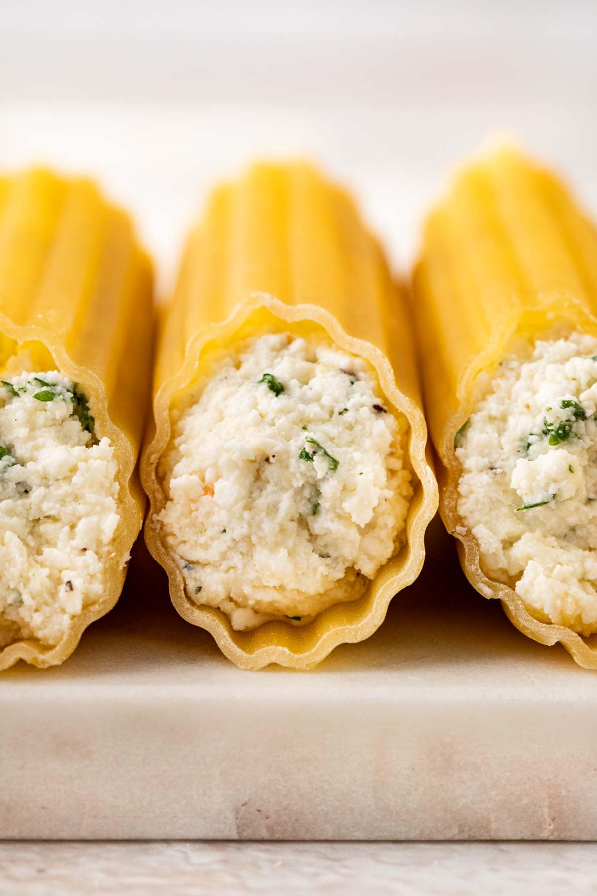 Cheesy Manicotti pasta tubes stuffed with cheese on cutting board side view