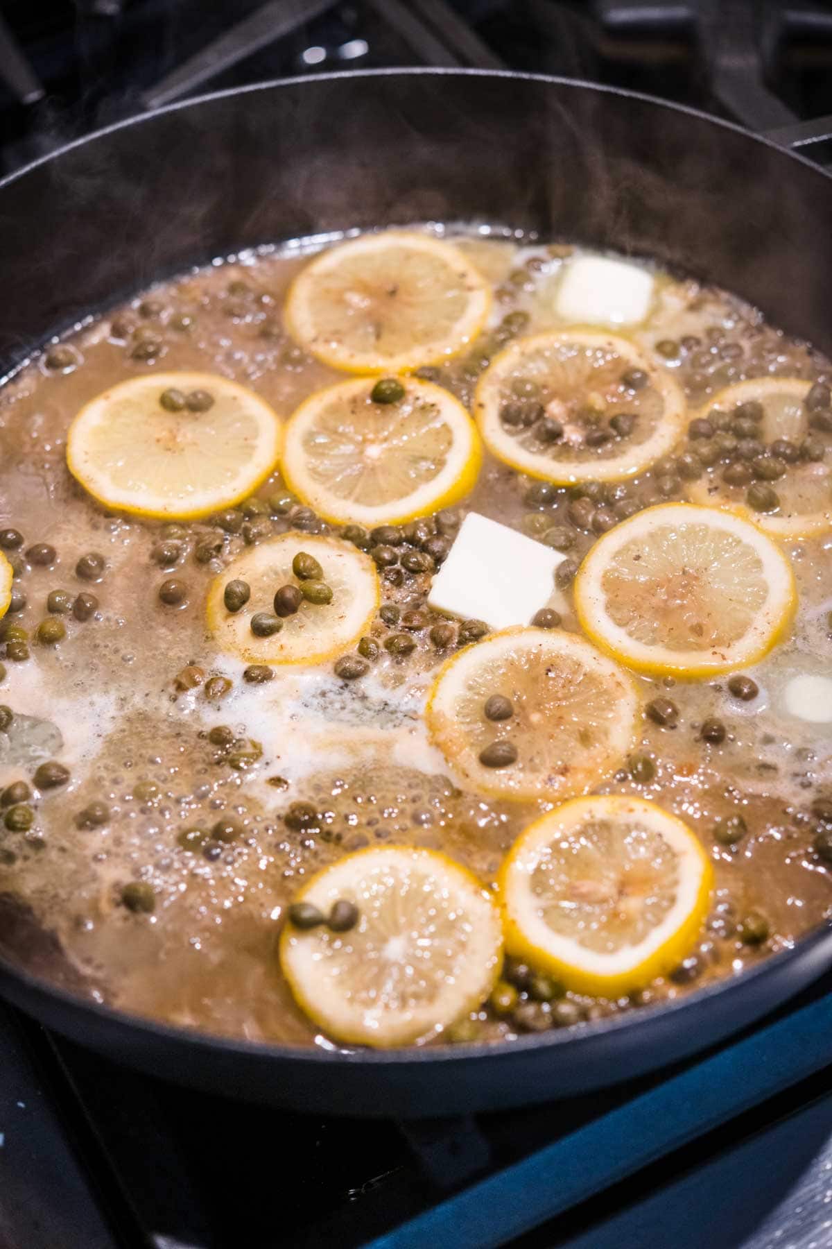 Lemon slices, butter, and capers simmering with stock in pan for Chicken Piccata