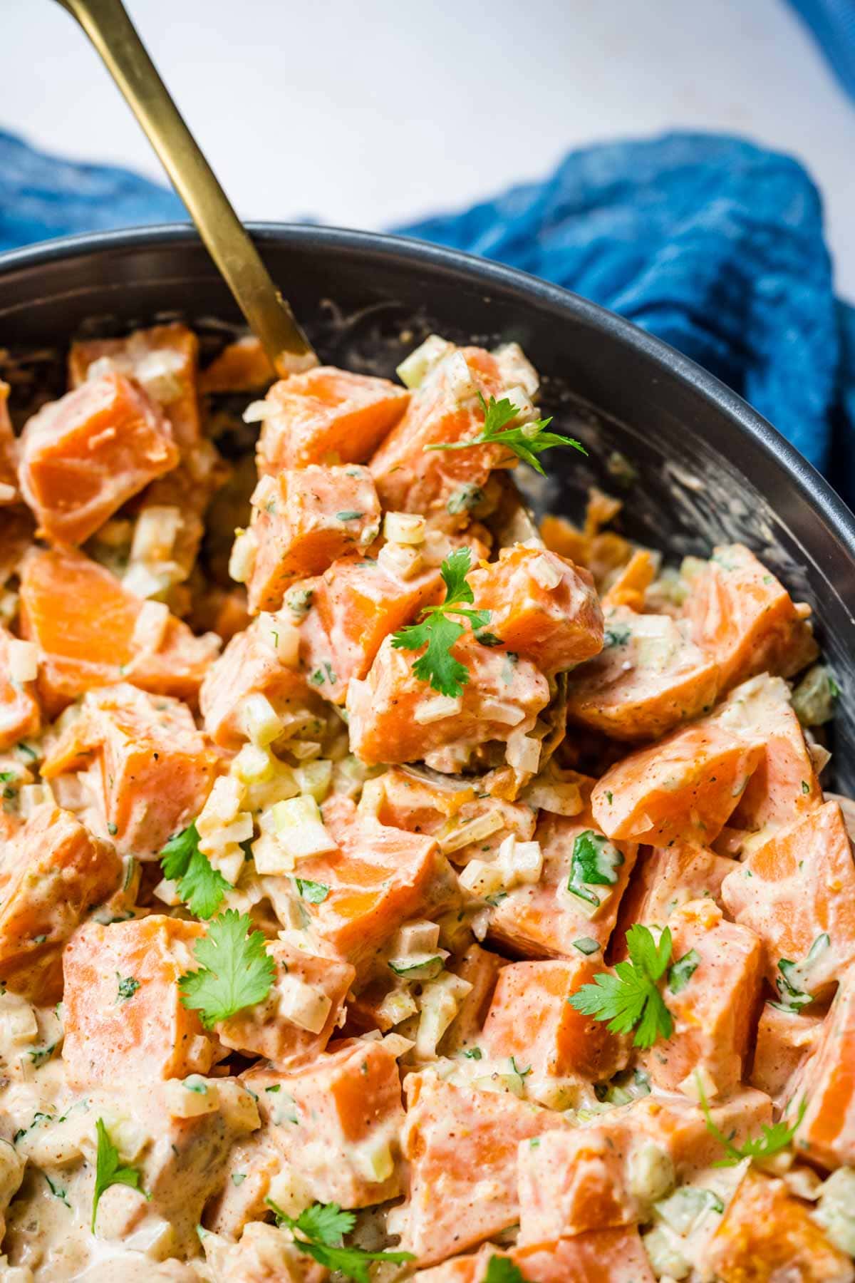 Creamy Spicy Sweet Potato Salad in serving bowl with spoon and cilantro garnish