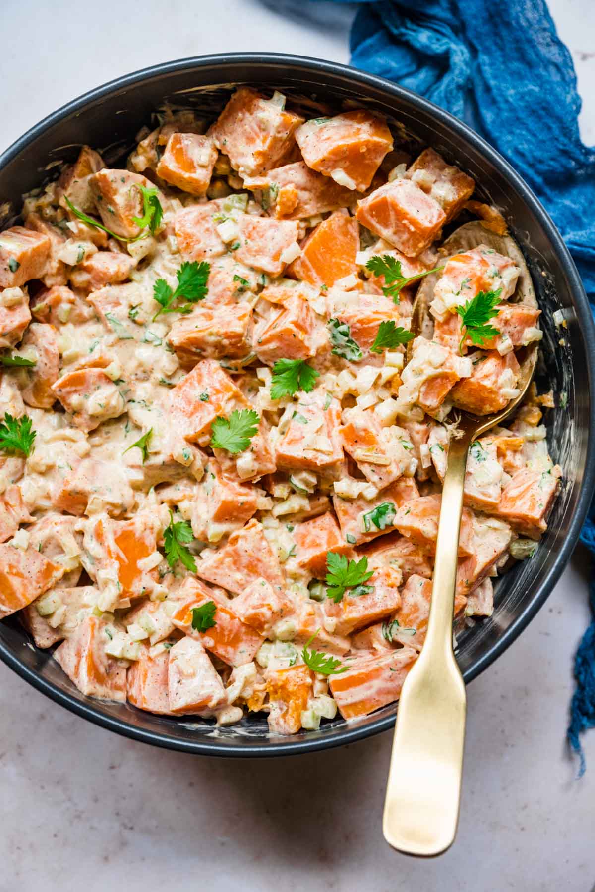 Creamy Spicy Sweet Potato Salad in serving bowl with spoon and cilantro garnish