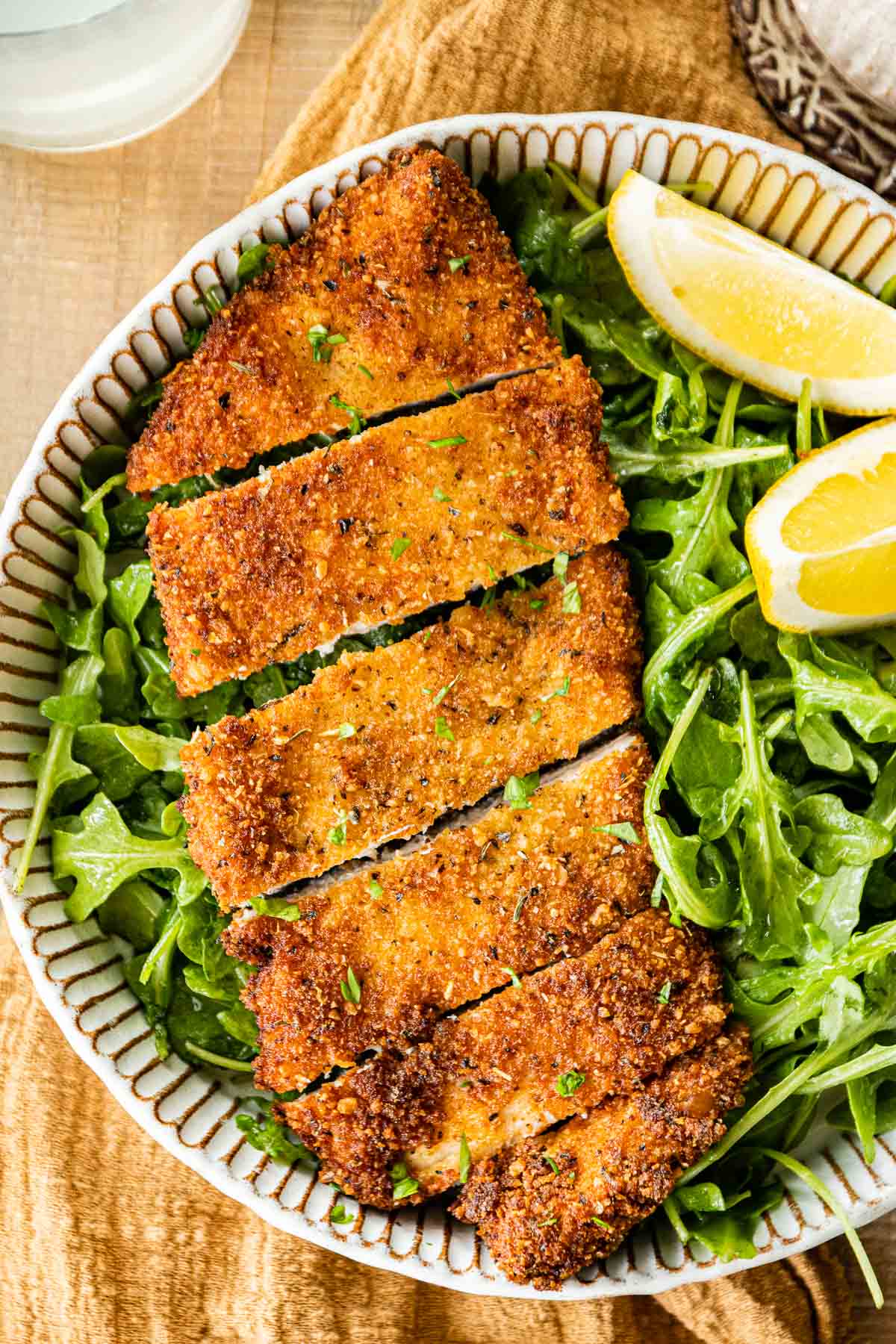 Crispy Breaded Chicken sliced on plate with greens and lemons