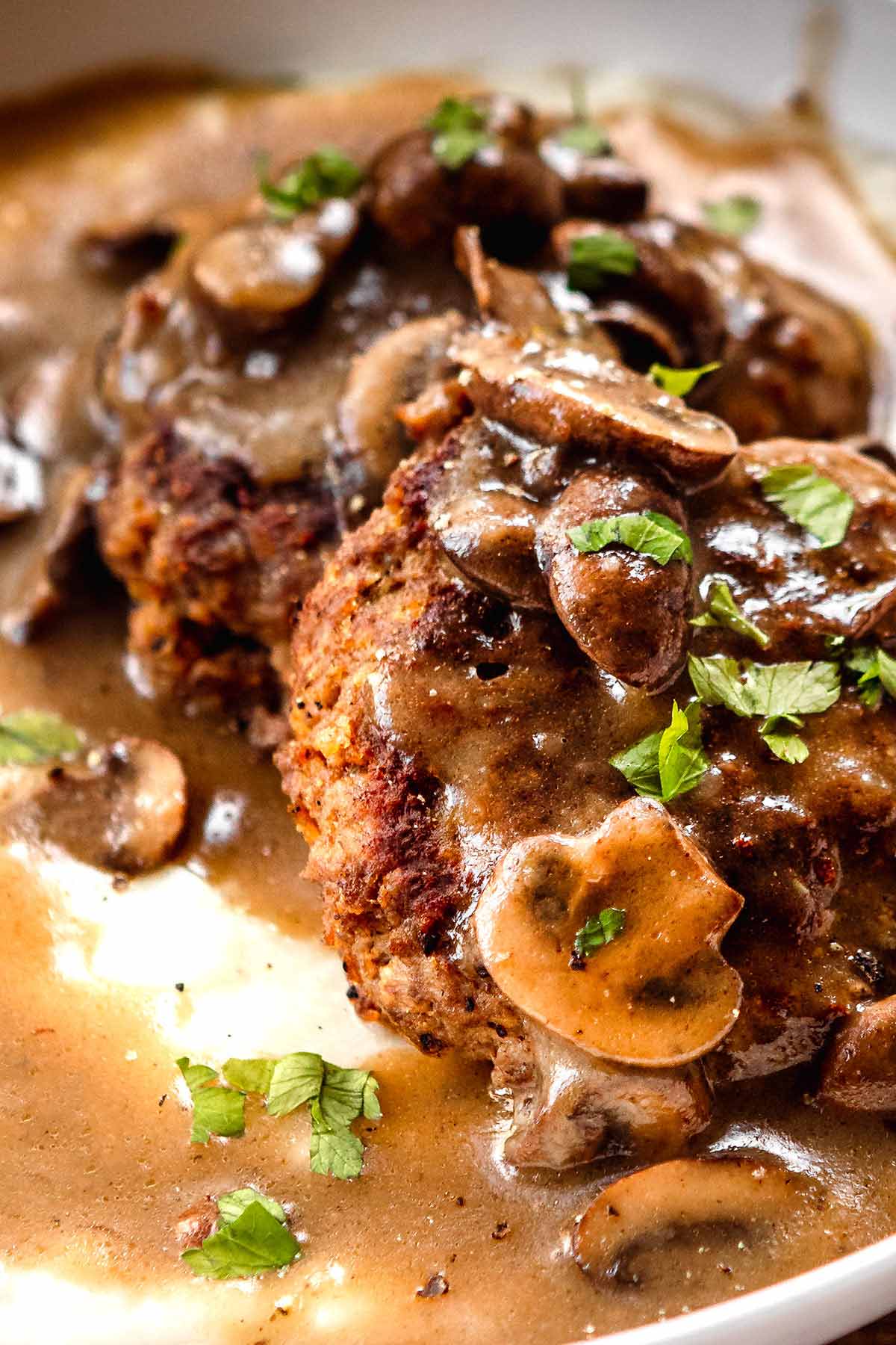 Hamburger Steaks with Mushroom Gravy served in a dish over mashed potatoes