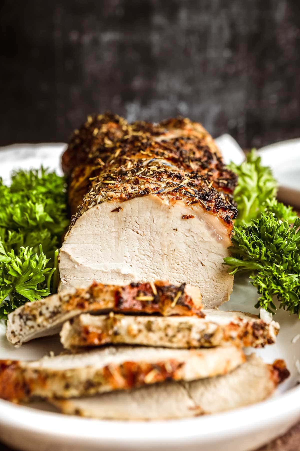 Herb Crusted Pork Loin sliced on platter with parsley garnish