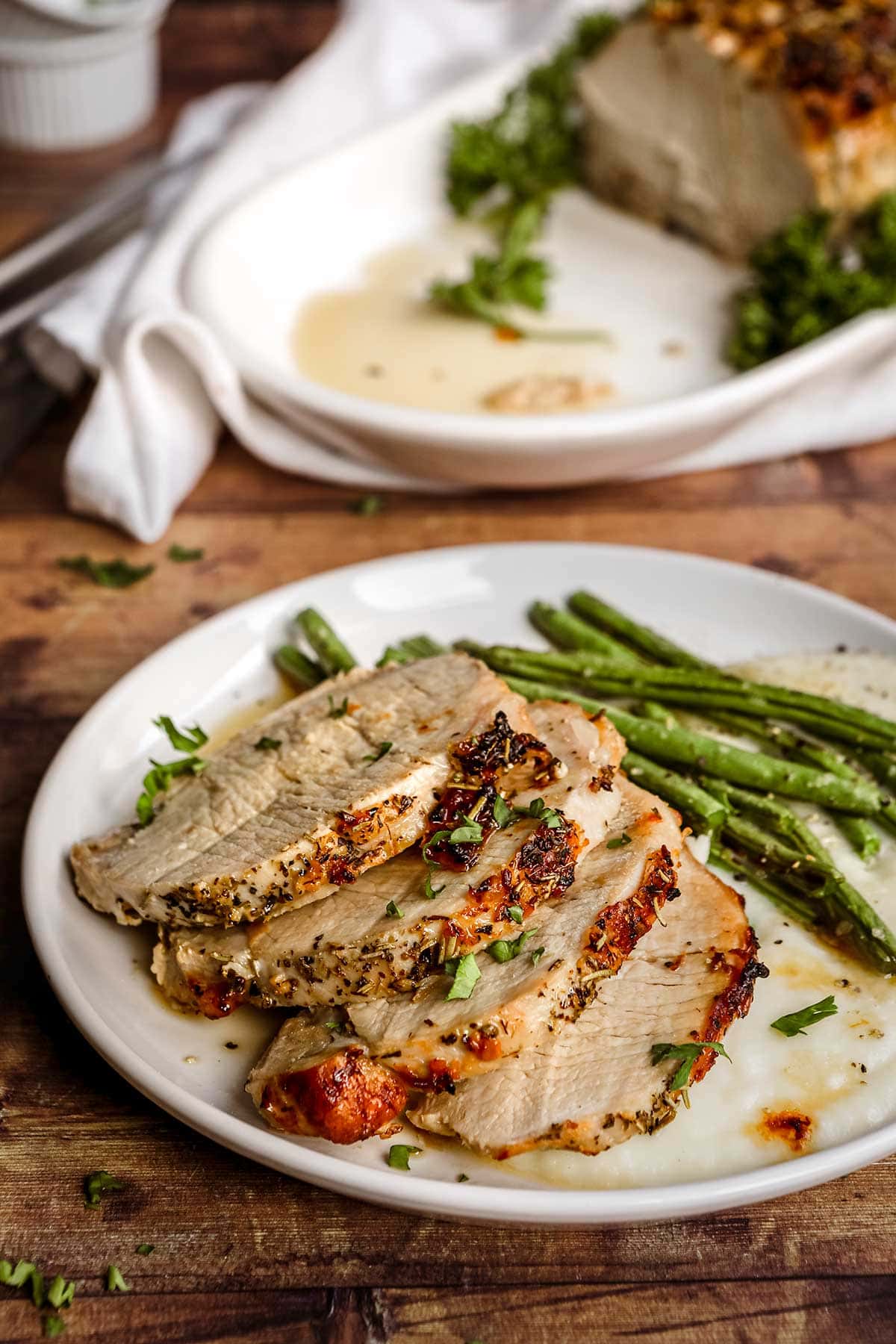 Herb Crusted Pork Loin sliced on plate with parsley garnish and green beans