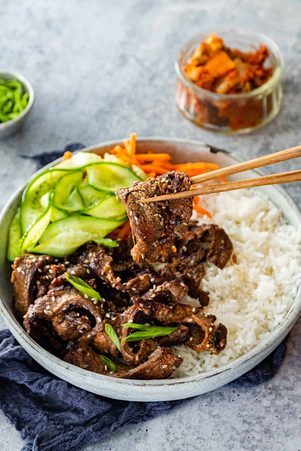 Korean Beef Bulgogi cooked beef slices in serving bowl with white rice, shredded carrots, and sliced cucumbers