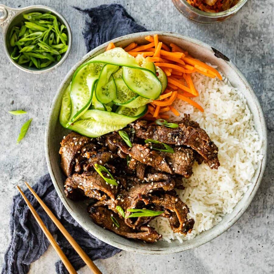 Korean Beef Bulgogi cooked beef slices in serving bowl with white rice, shredded carrots, and sliced cucumbers