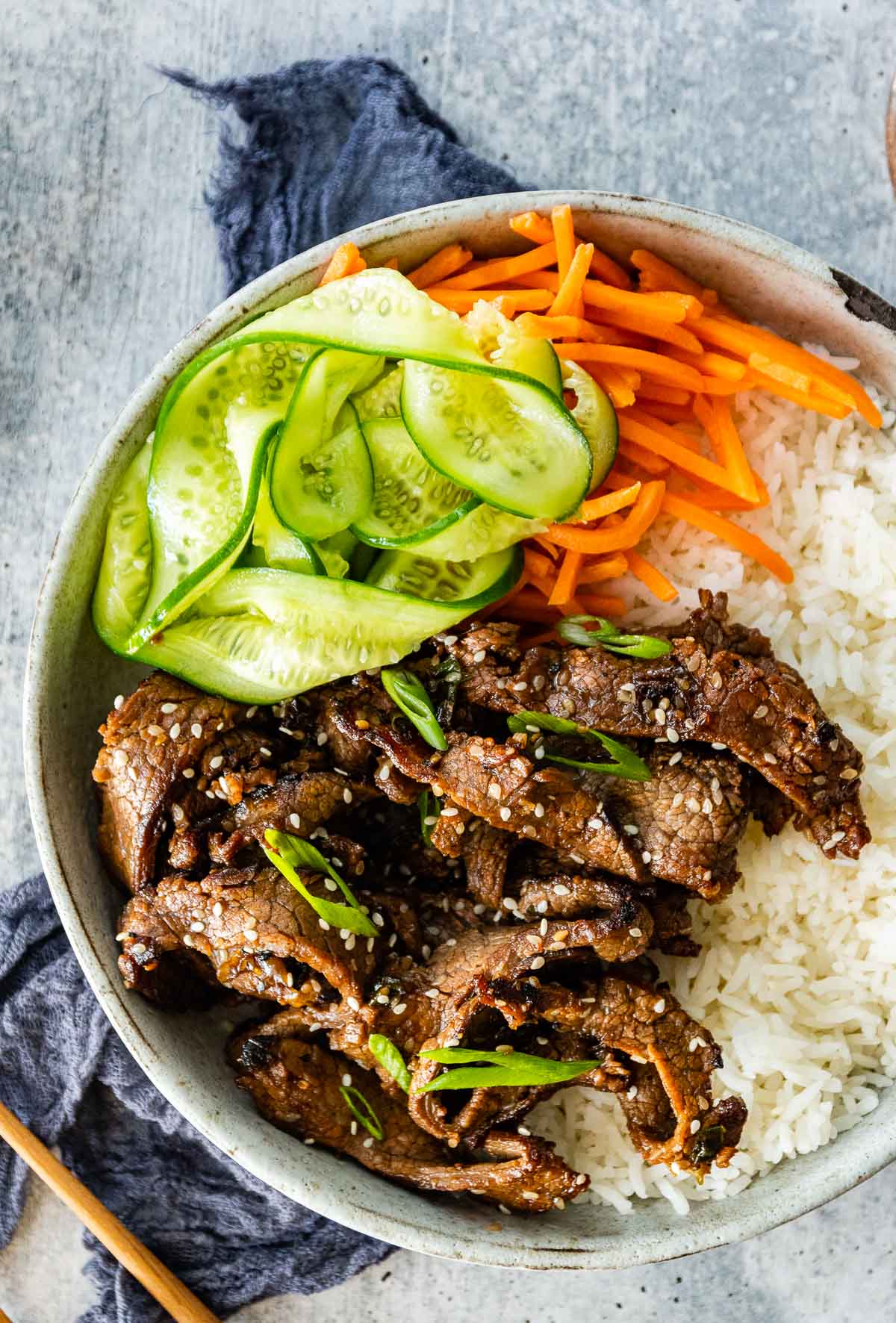 Korean Beef Bulgogi cooked beef slices in serving bowl with white rice, shredded carrots, and sliced cucumbers