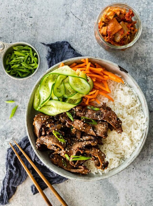 Korean Beef Bulgogi cooked beef slices in serving bowl with white rice, shredded carrots, and sliced cucumbers